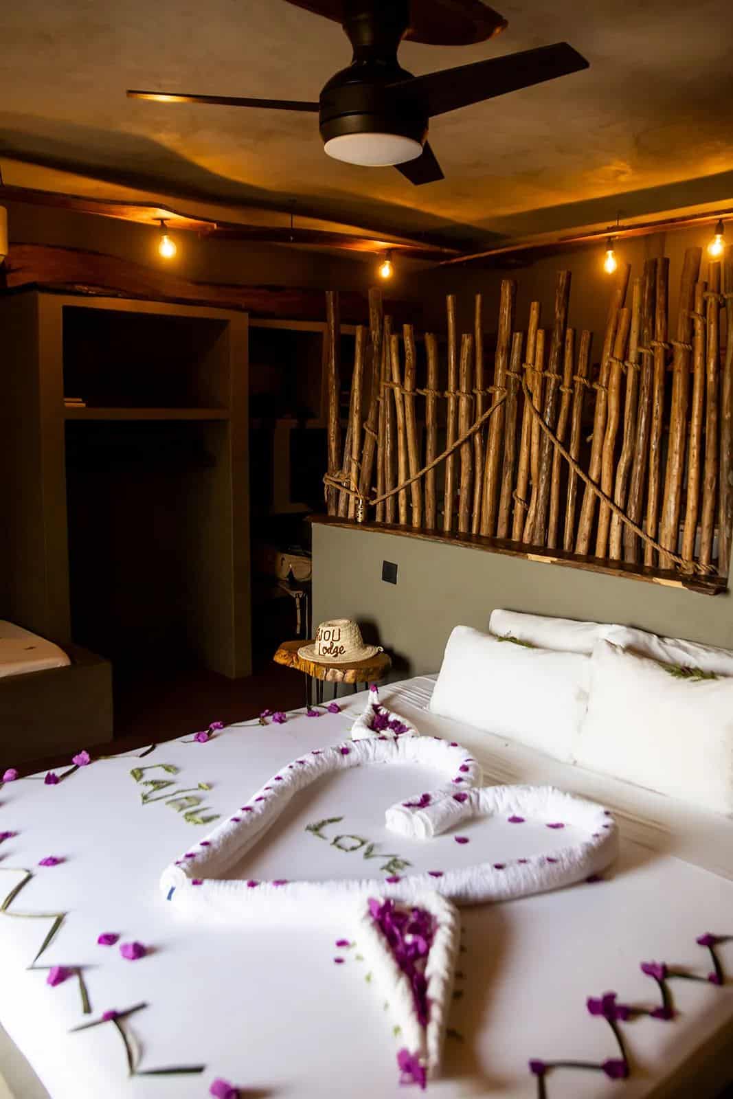 Cajou Lodge room rates: bed with flower petals and wooden headboard